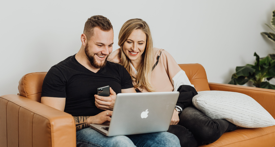 Smilende mand og kvinde sidder sammen i en brun sofa og har lige fået deres mobile bredbånd fra Velkommen op at køre 
