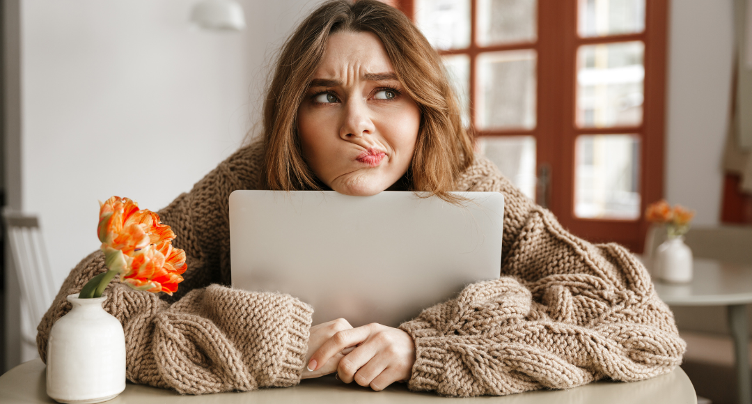 Pige i brun striktrøje sidder med en computer mellem armene og ser forvirret ud fordi hun prøver at forstå sin elregning