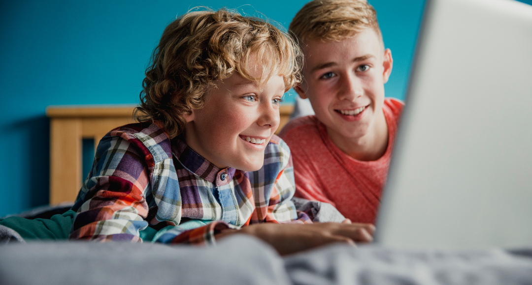 To smilende drenge, der sidder ved en computer på mobilt bredbånd fra Velkommen 