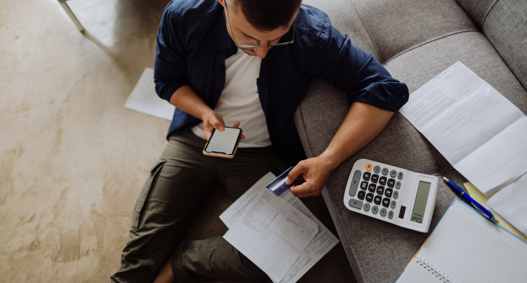 Mand med briller, der holder sit dankort i blandt nogle regninger og undrer sig over, hvorfor han har modtaget to naturgasregninger fra Velkommen og ikke kun én.png