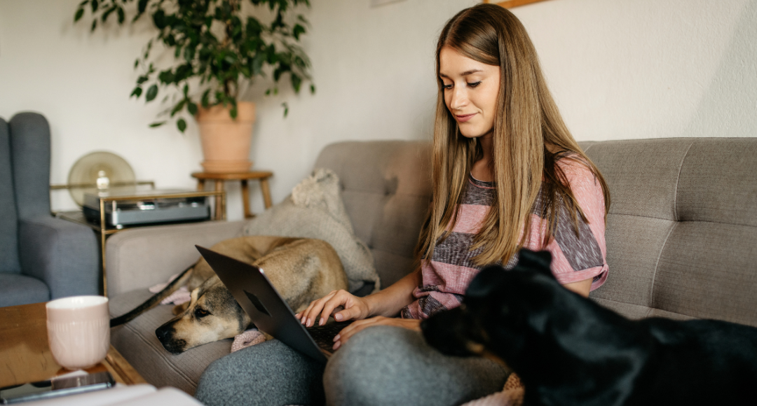 Pige i stribet trøje sidder i sofa med to hunde og tjekker sine mobilregninger fra velkommen