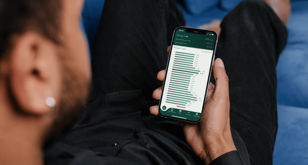 Person ligger i sofa med telefon i hånden og er logget ind på velkommens app, hvor han følger elpriserne time for time