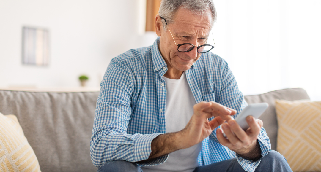 ældre mand med briller i blå ternet skjorte, der på sin mobil kigger på sin elregning fra velkommen for at forstå hvad han egentligt betaler for