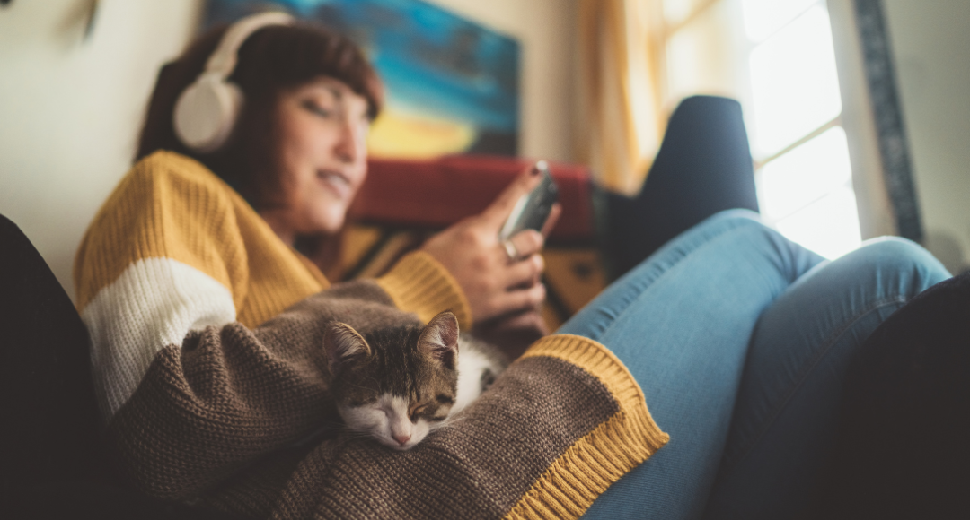 Pige med høretelefoner på slapper af med sin kat liggende på skødet, imens hun tjekker timerpriserne på el på velkommens hjemmeside.png