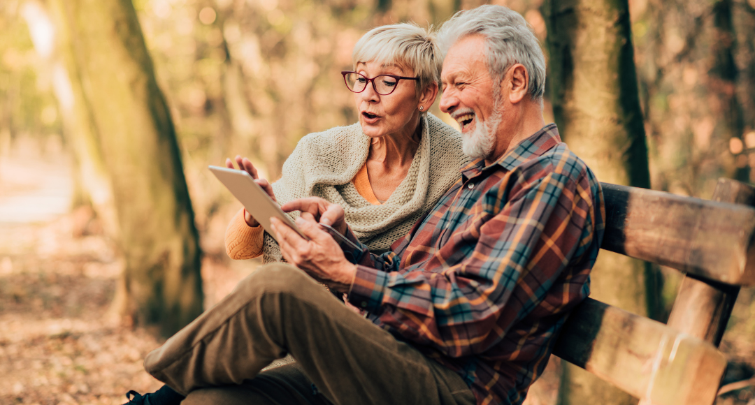 Ældre ægtepar der sidder i naturen og gør brug af mobilt bredbånd på deres iPad