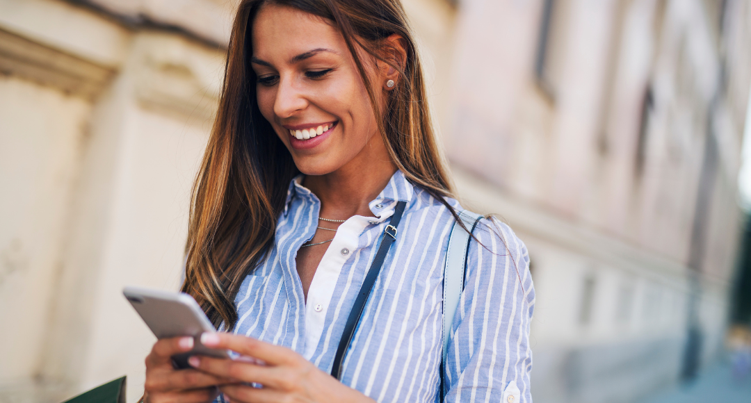 kvinde i blå skjorte der smiler med sin mobil i hænderne og gør brug af velkommens hurtige data i udlandet 